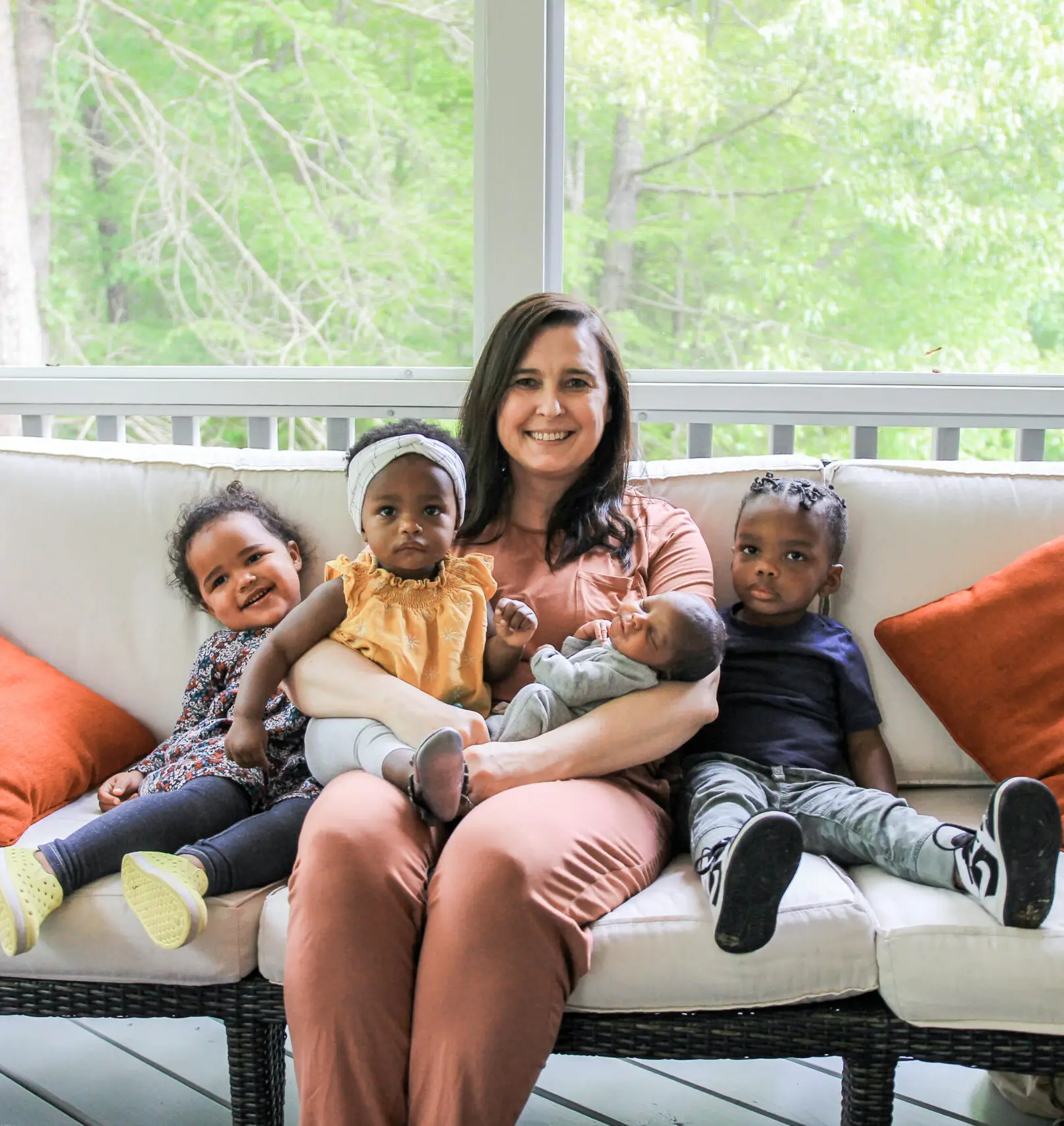 Adoption agency owner, Tammy Davis, sits with three little children on a white couch on a porch.